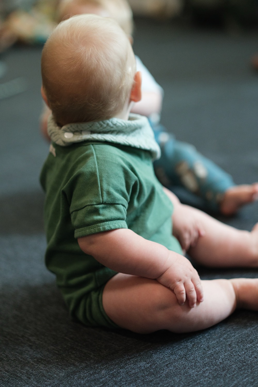 A baby sitting on the floor at the pilot while the grown-ups learn